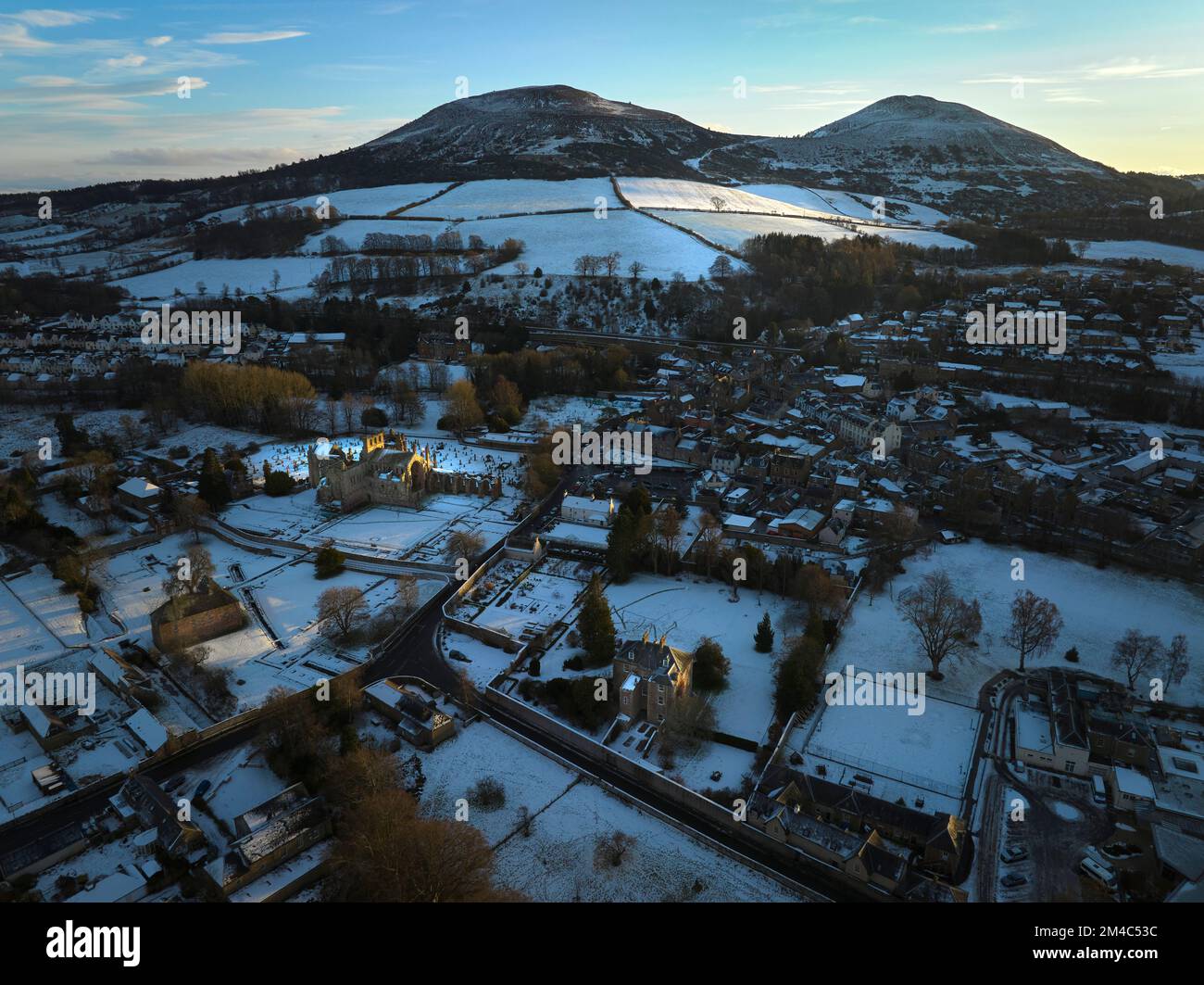 Luftaufnahme von Melrose Abbey, Harmony House und den Eildons mit einer Schicht Schnee und Frost bei Sonnenuntergang an einem frischen Wintertag im Dezember. Stockfoto