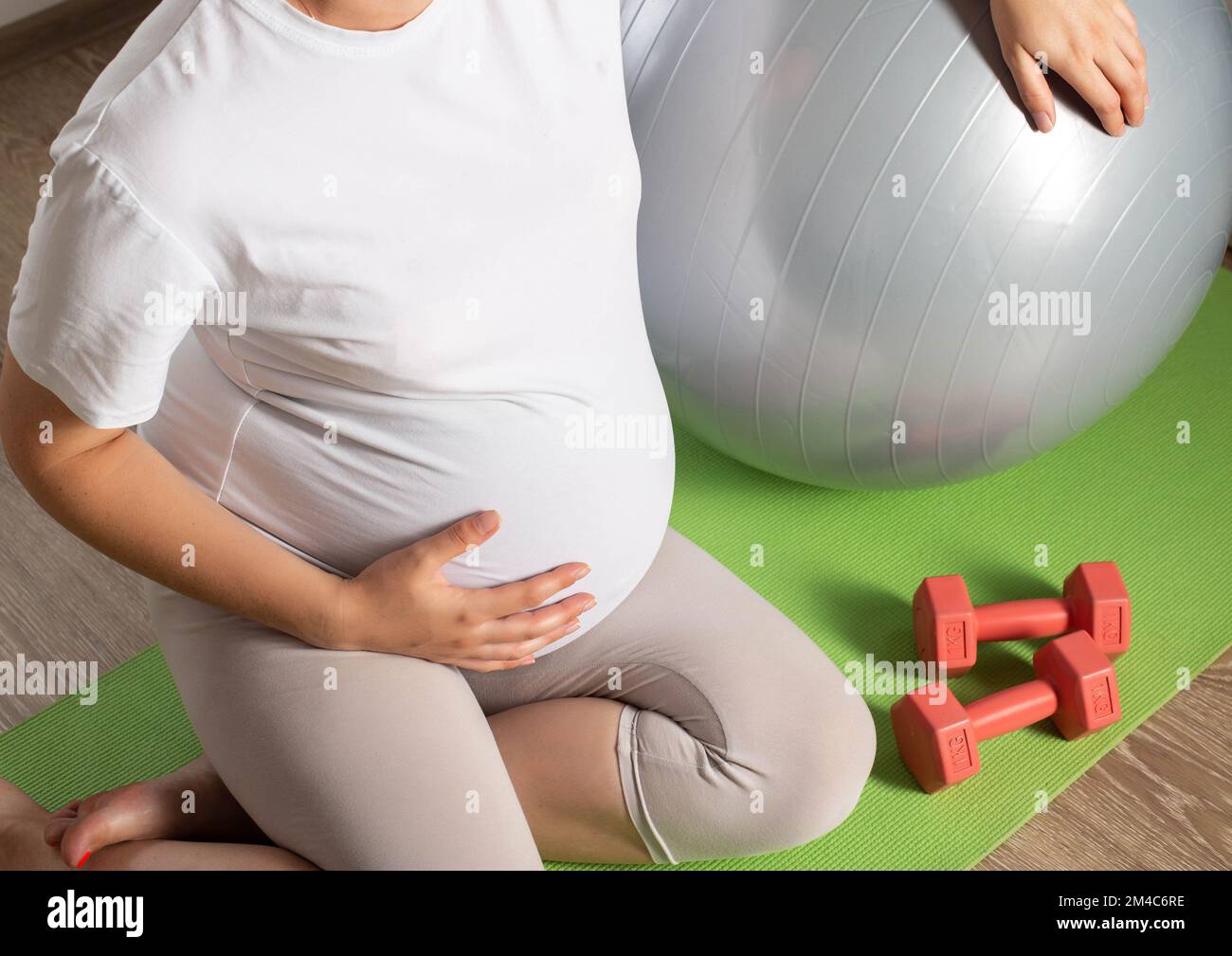 Eine schwangere Frau mit einem großen Bauch ist mit Kurzhanteln vor dem