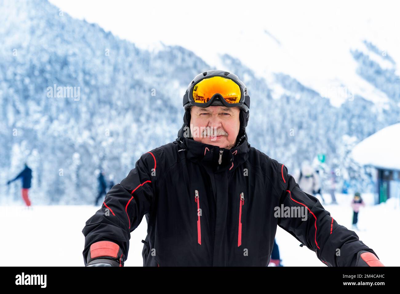 Aktiver Senior erfahrener alter Mensch in Skihelm, Schutzbrille und schwarzem Anzug vor malerischem Panorama-Gipfel Genießen Sie kalten Extremsport Stockfoto