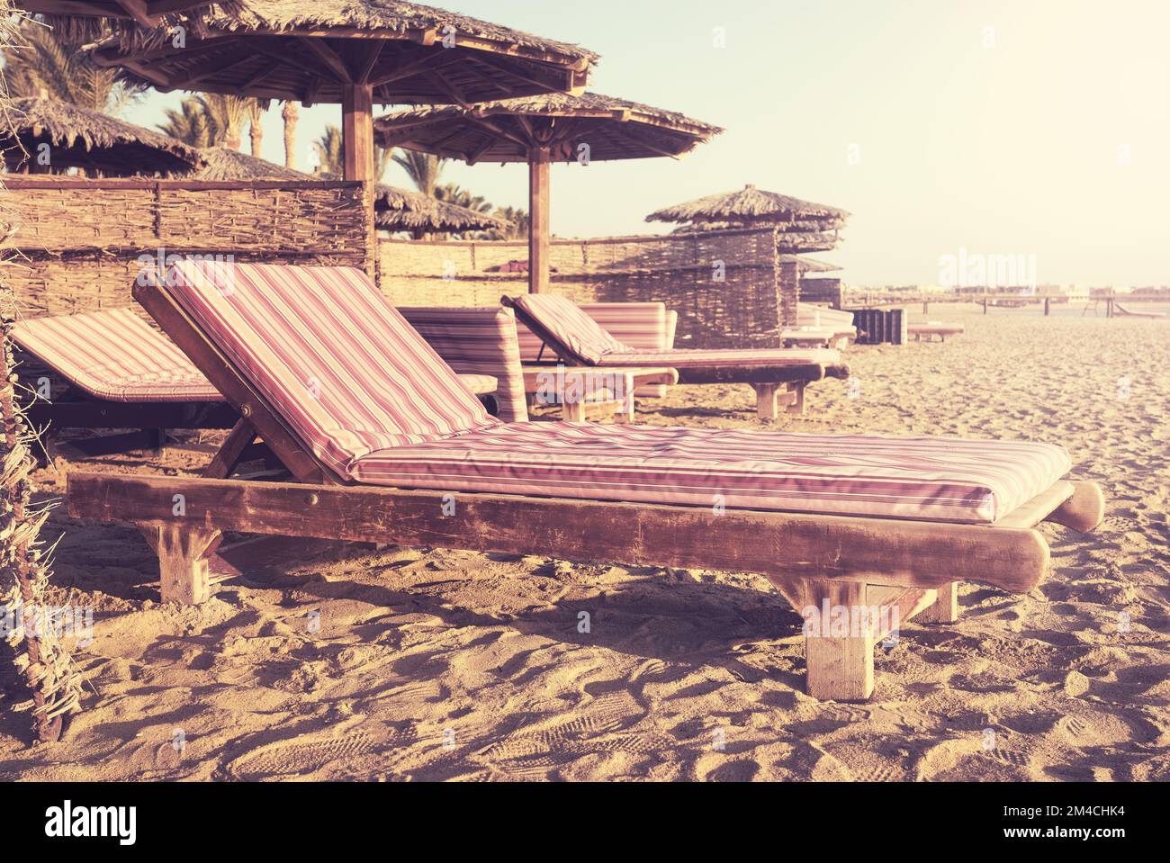 Retro-Bild eines tropischen Strandes mit Holzliegen und Sonnenschirmen, Sommerurlaubskonzept. Stockfoto