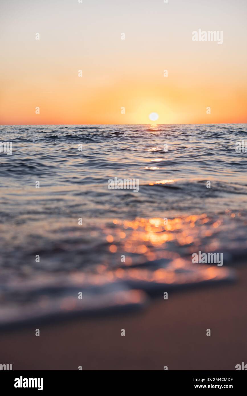 Wenn die Sonne untergeht, strahlt sie ein warmes Licht aus, während die Wellen sanft hereinrollen. Stockfoto