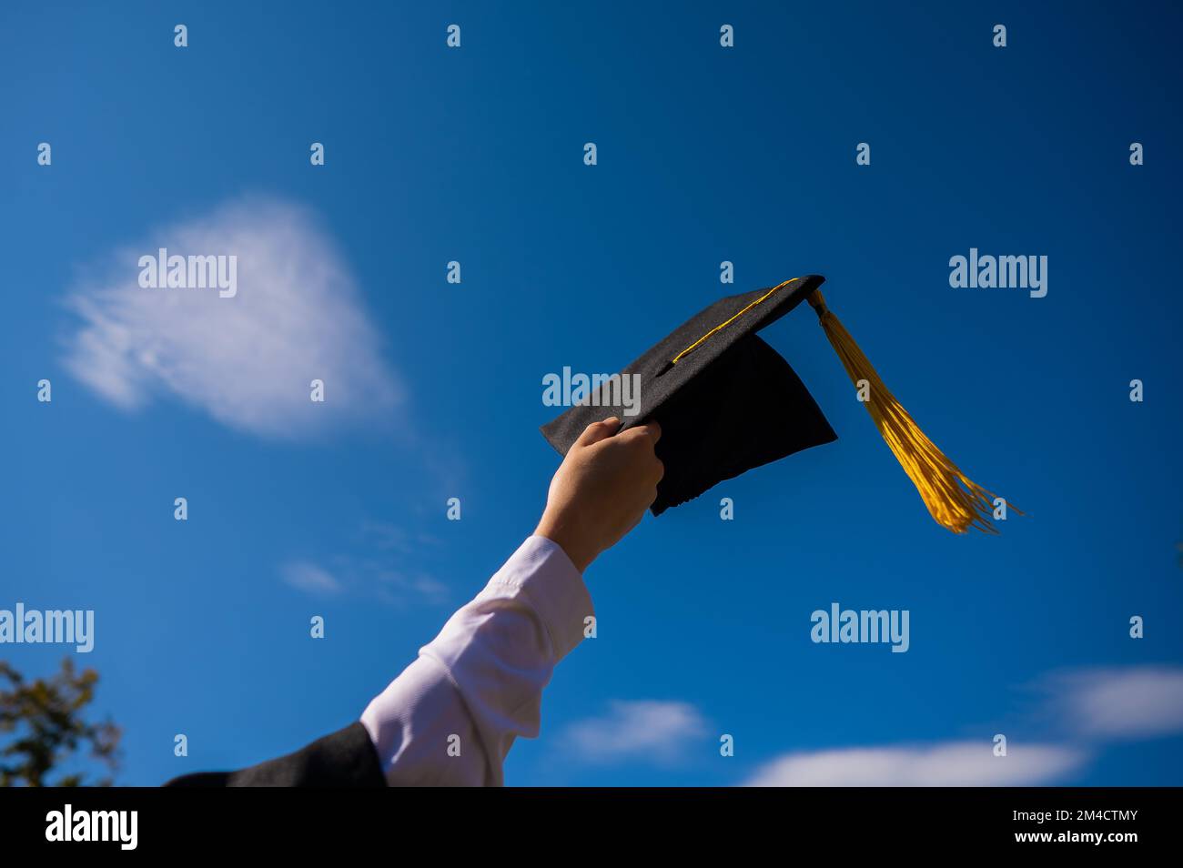 Nahaufnahme einer Frauenhand mit Abschlusskappe am blauen Himmel. Stockfoto