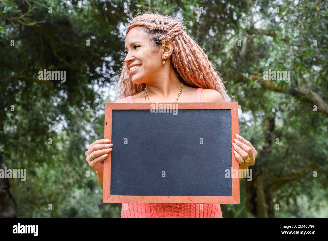 Eine lateinische Frau, die eine Tafel hält und nach links in einem Park schaut Stockfoto