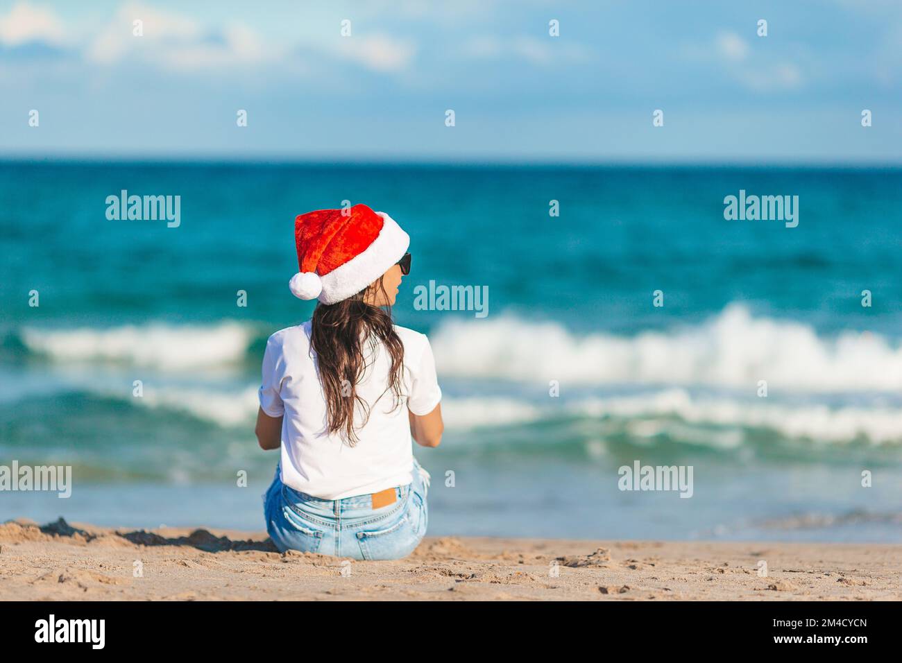 Junge Frau mit Weihnachtsmann-Hut an Weihnachten am Strand Stockfoto