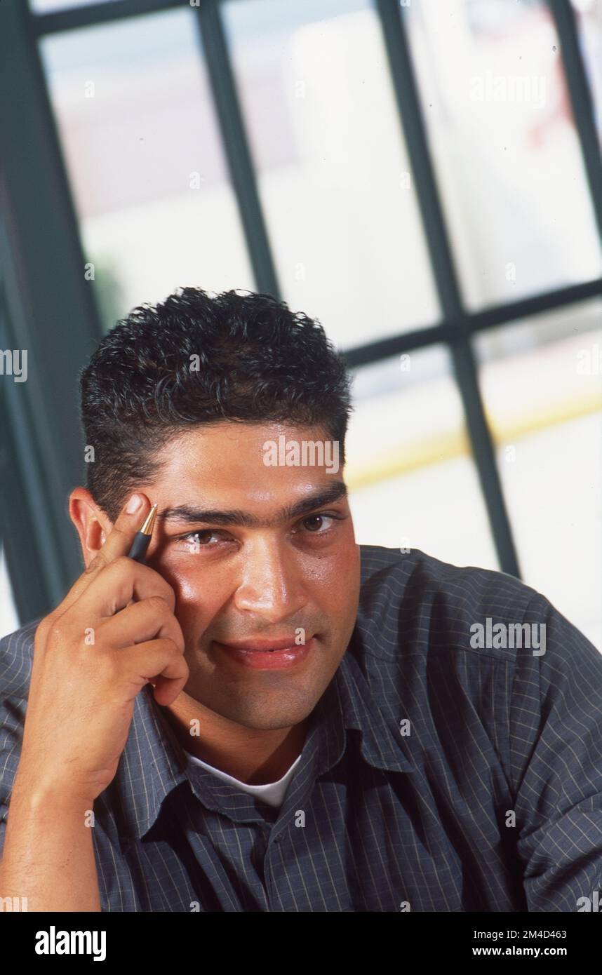 Nahaufnahme eines jungen Mannes, der sich mit einem Stift auf die Hand lehnt und in die Kamera schaut Stockfoto
