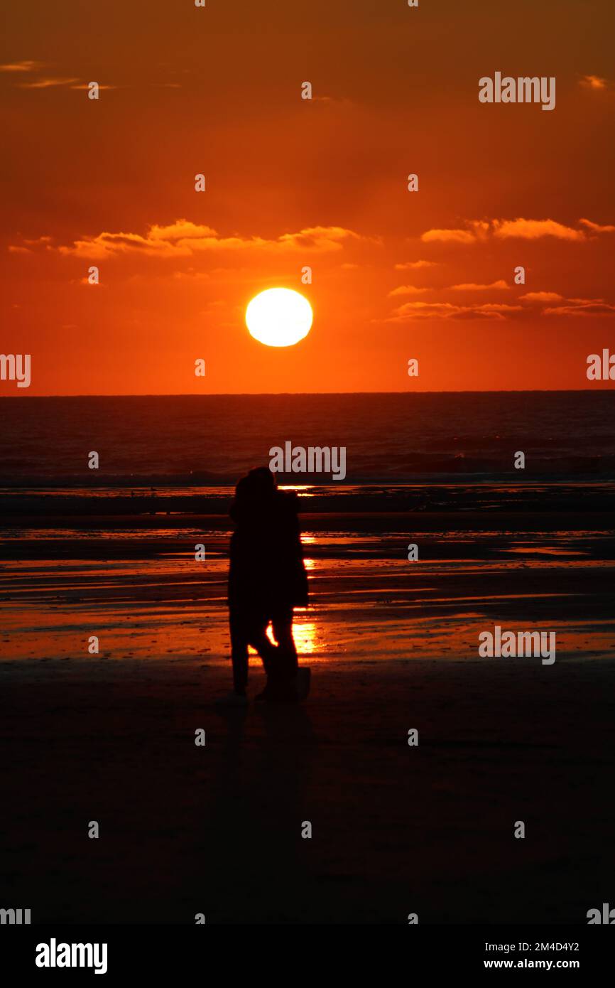 Eine vertikale Aufnahme eines fantastischen Sonnenuntergangs mit einem Paar, das am Strand von Hardelot, Frankreich, spaziert Stockfoto