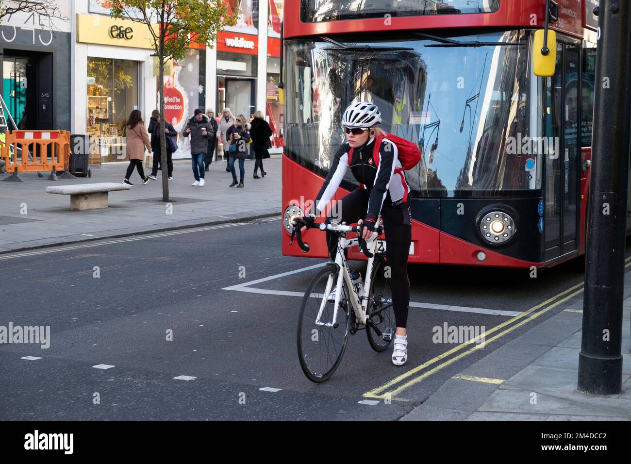 Junge Radfahrerin, die an der Ampel vor einem roten Doppeldeckerbus auf der Oxford Street West End London England KATHY DEWITT wartet Stockfoto