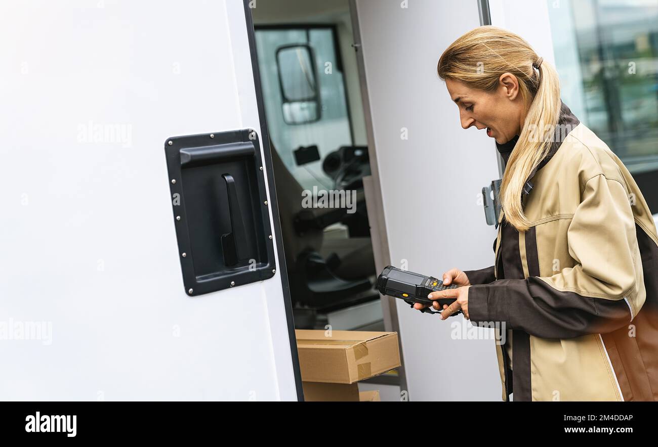 Ein Lieferagent hält den Strichcode-Scanner vor ihrem Van, um die Pakete zu überprüfen Stockfoto