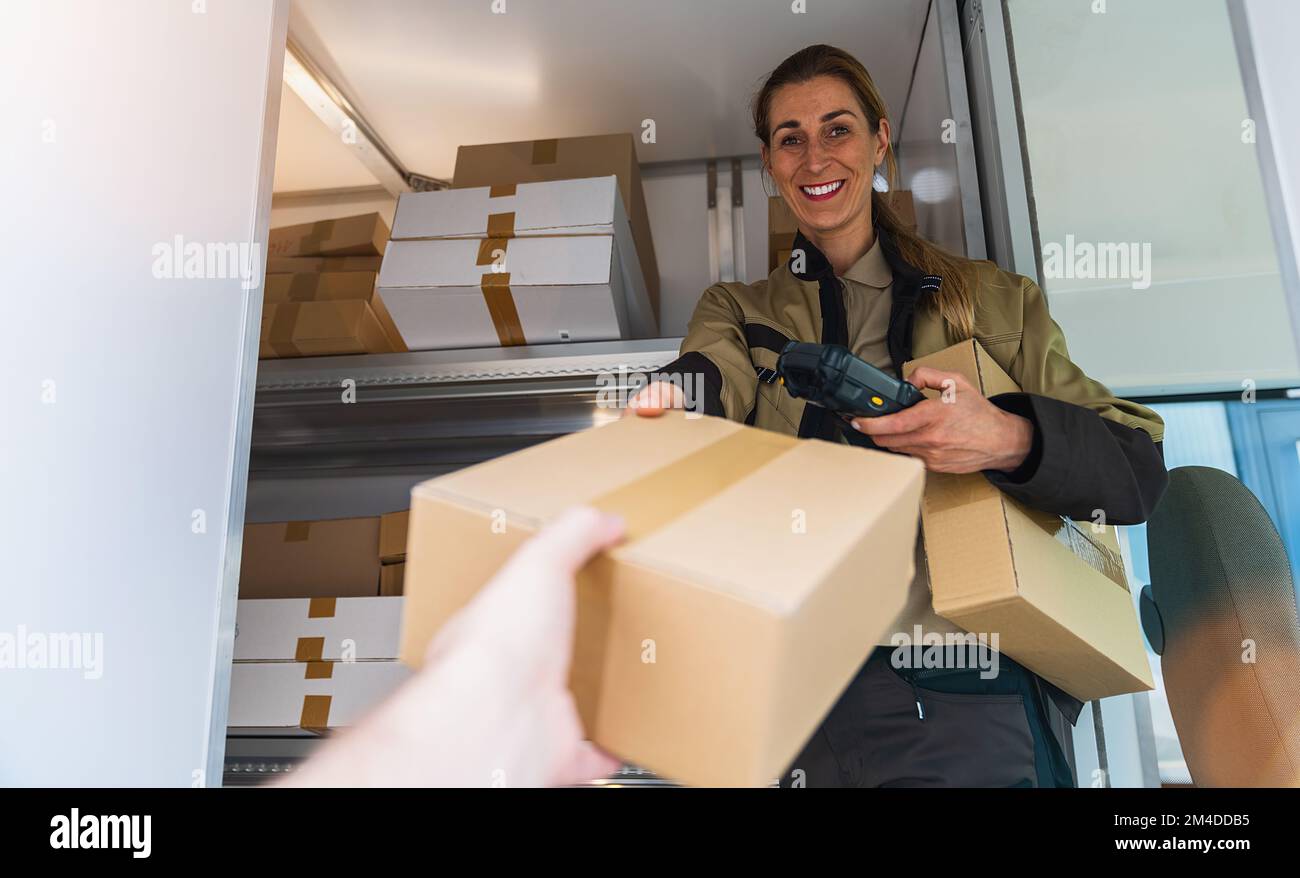 Eine Lieferagentin übergibt ein Paket in ihrem Lieferwagen, um es an einen Kunden zu liefern Stockfoto