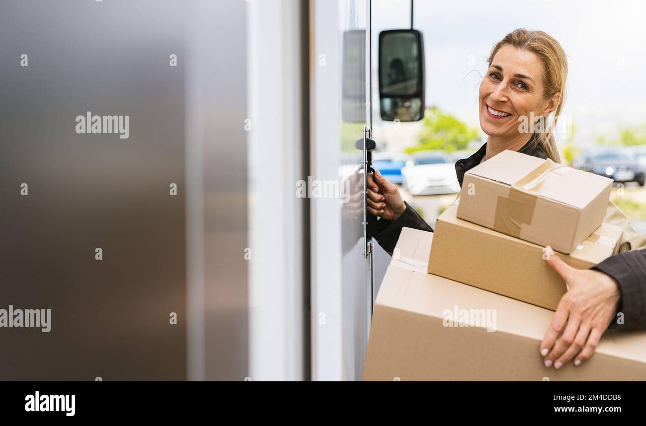 Lächelnde weibliche Lieferantin hält Pakete vor einem Lieferwagen, um sie an einen Kunden zu liefern, mit Platz für individuellen Text Stockfoto