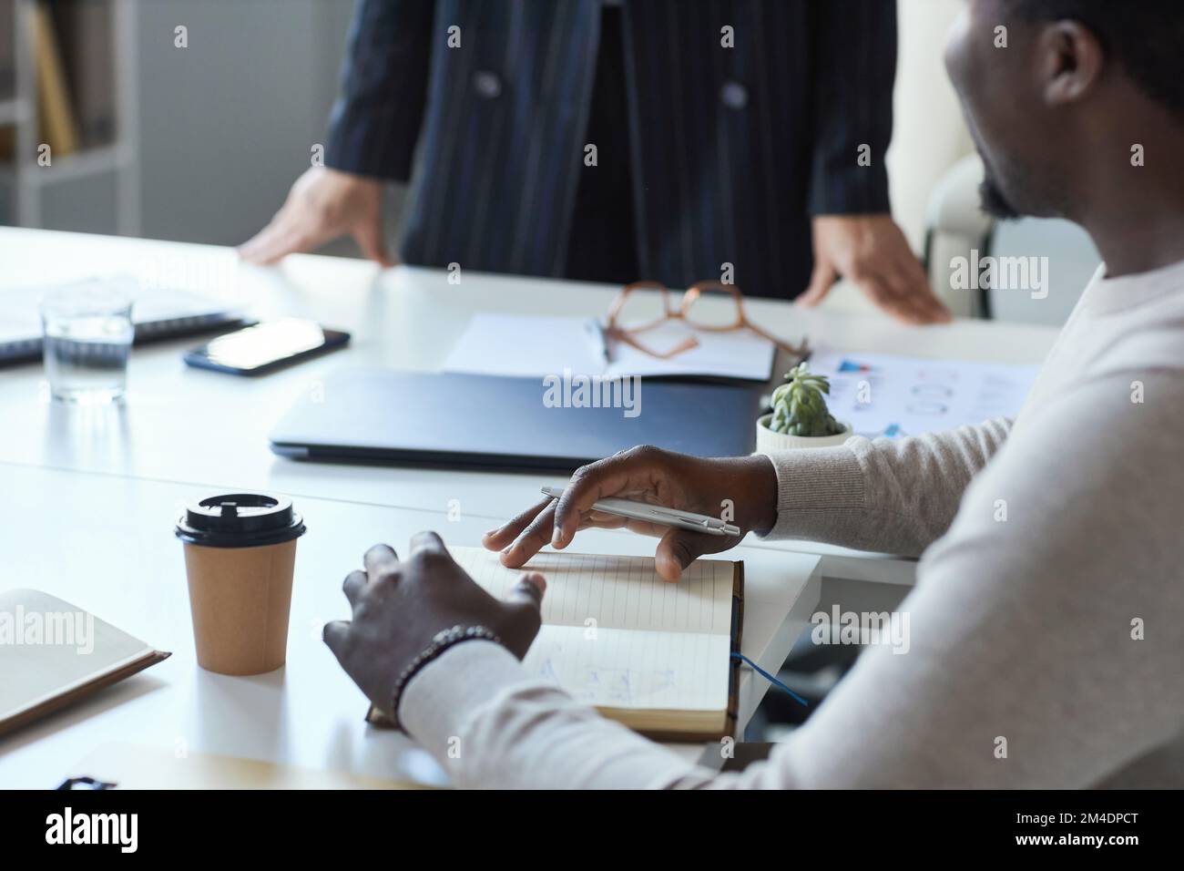 Nahaufnahme eines schwarzen Mannes, der sich während des Geschäftstreffens mit dem Team Notizen im Planer macht Stockfoto