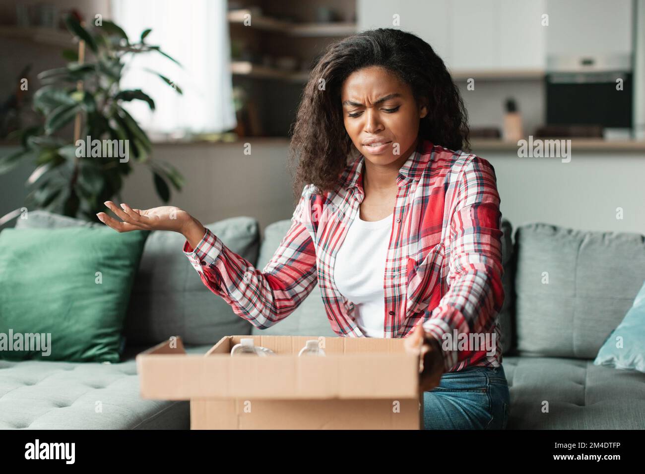 Schockierte, wütende Millenials schwarze Frau, die Pappkartons auspackt, Geste im Wohnzimmer Stockfoto
