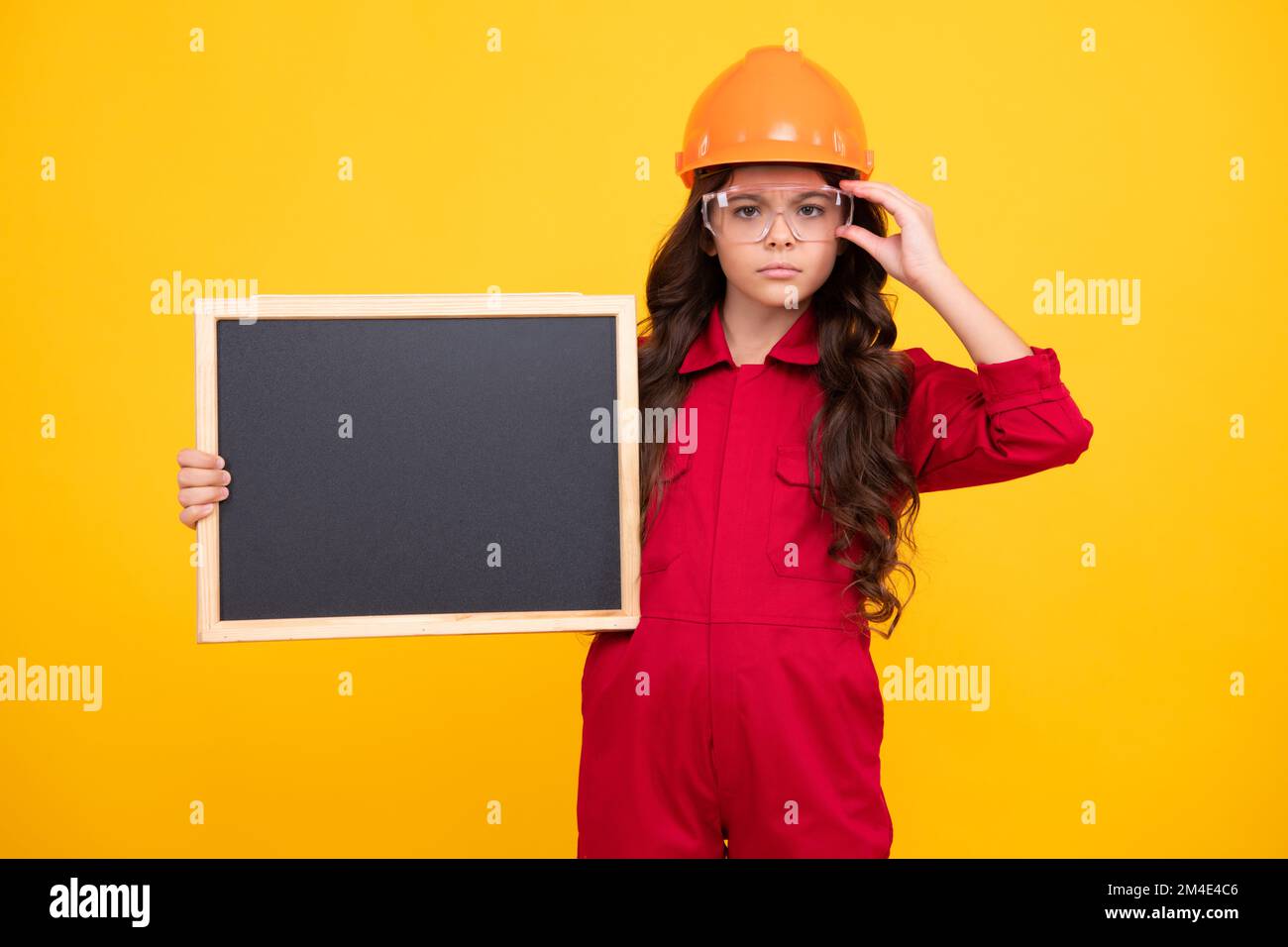 Kind Mädchen Baumeister in Harthut Helm. Teenagermädchen halten die Tafel auf gelbem Hintergrund isoliert. Renovierungskonzept für Kinder. Platz kopieren, Modell erstellen Stockfoto