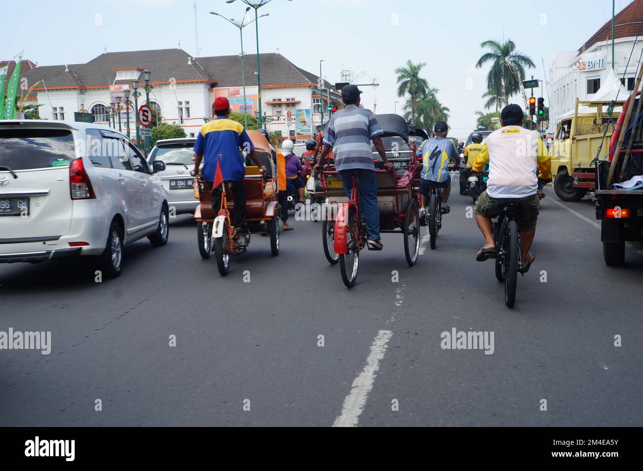 Eine Gruppe von Radfahrern, Rikschas, die am 2017. Mai zwischen Autos auf der Straße von Yogyakarta, Indonesien, unterwegs sind Stockfoto