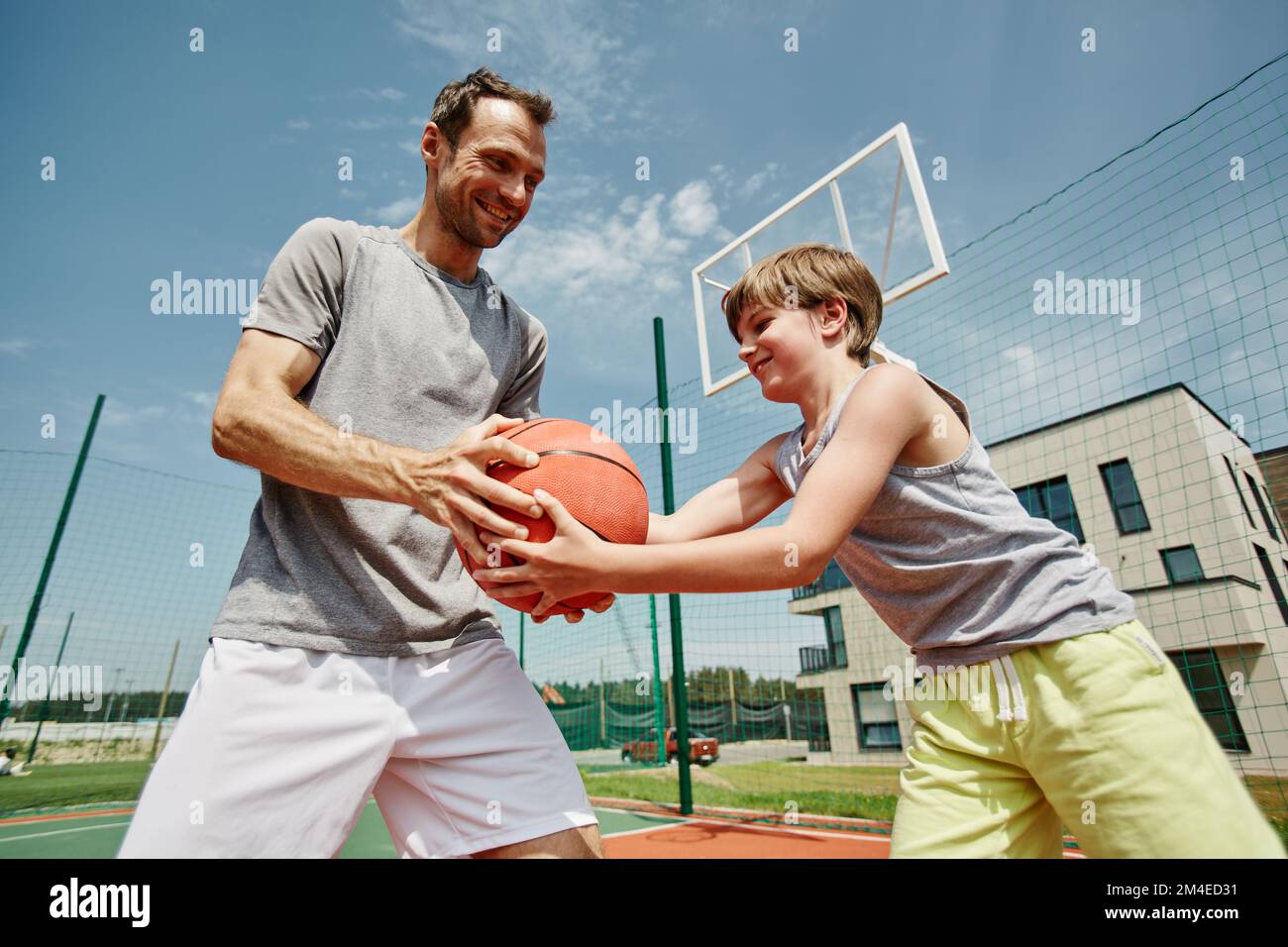 Seitliches Porträt von Vater und Sohn, die zusammen Basketball spielen und glücklich lächeln Stockfoto