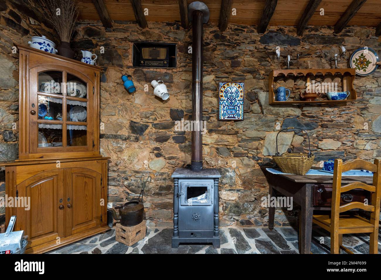 Kleiner Holzofen im Speisesaal eines rustikalen alten Landhauses mit Schieferwänden und Steinfußboden Stockfoto