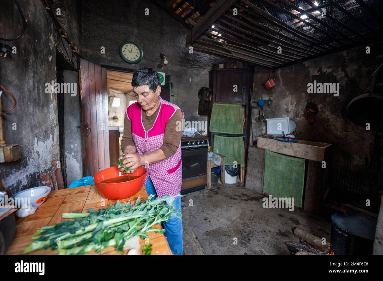 Eine Frau, die am offenen Feuer in einer kleinen, altmodischen Küche in einem Landhaus kocht Stockfoto