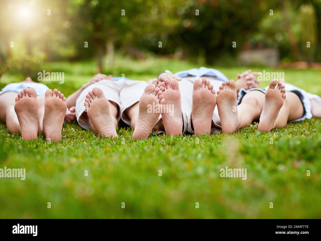 Die Füße hoch. Eine Gruppe von nicht wiedererkennbaren Menschen, die tagsüber mit den Füßen nach oben auf dem Rasen in einem Park lagen. Stockfoto