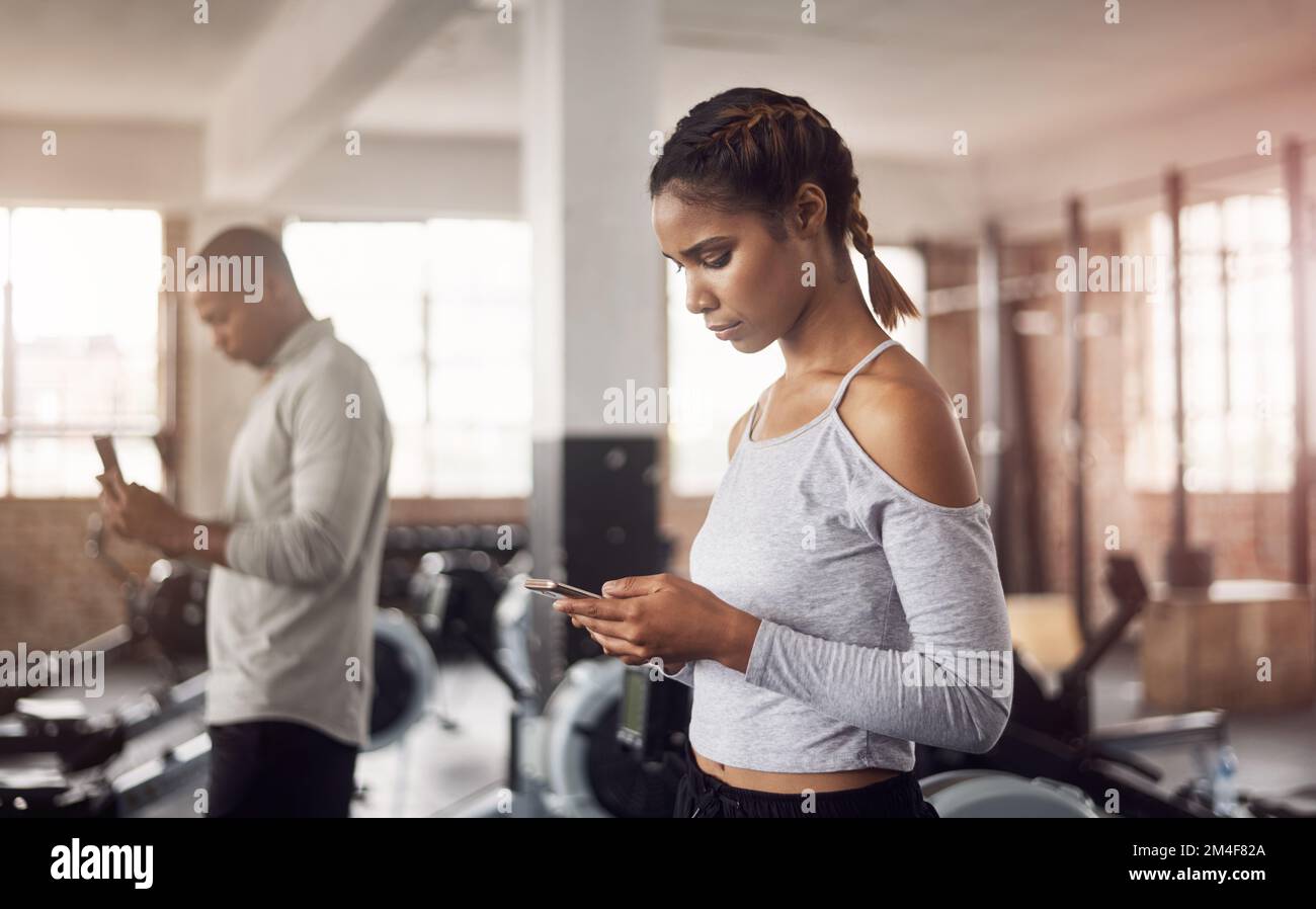 Die intelligenteste Art, deine Workouts aufzuzeichnen. Eine junge Frau, die ihre Smartphones in einem Fitnessstudio benutzt. Stockfoto