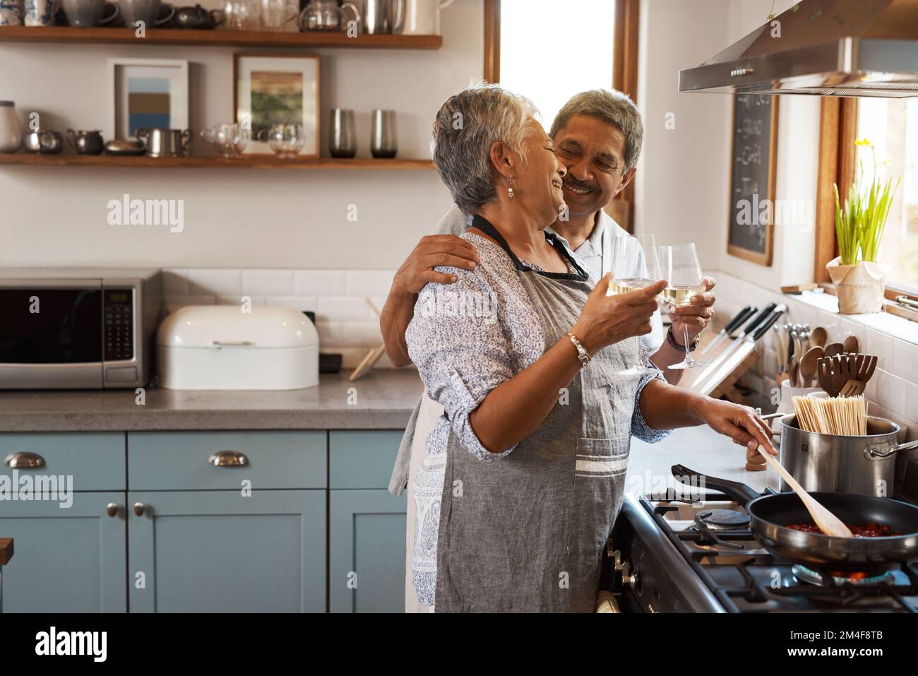 Wein passt am besten zu Romantik. Ein glückliches, reifes Paar, das mit Wein anstoßen und zu Hause zusammen eine Mahlzeit kochen. Stockfoto