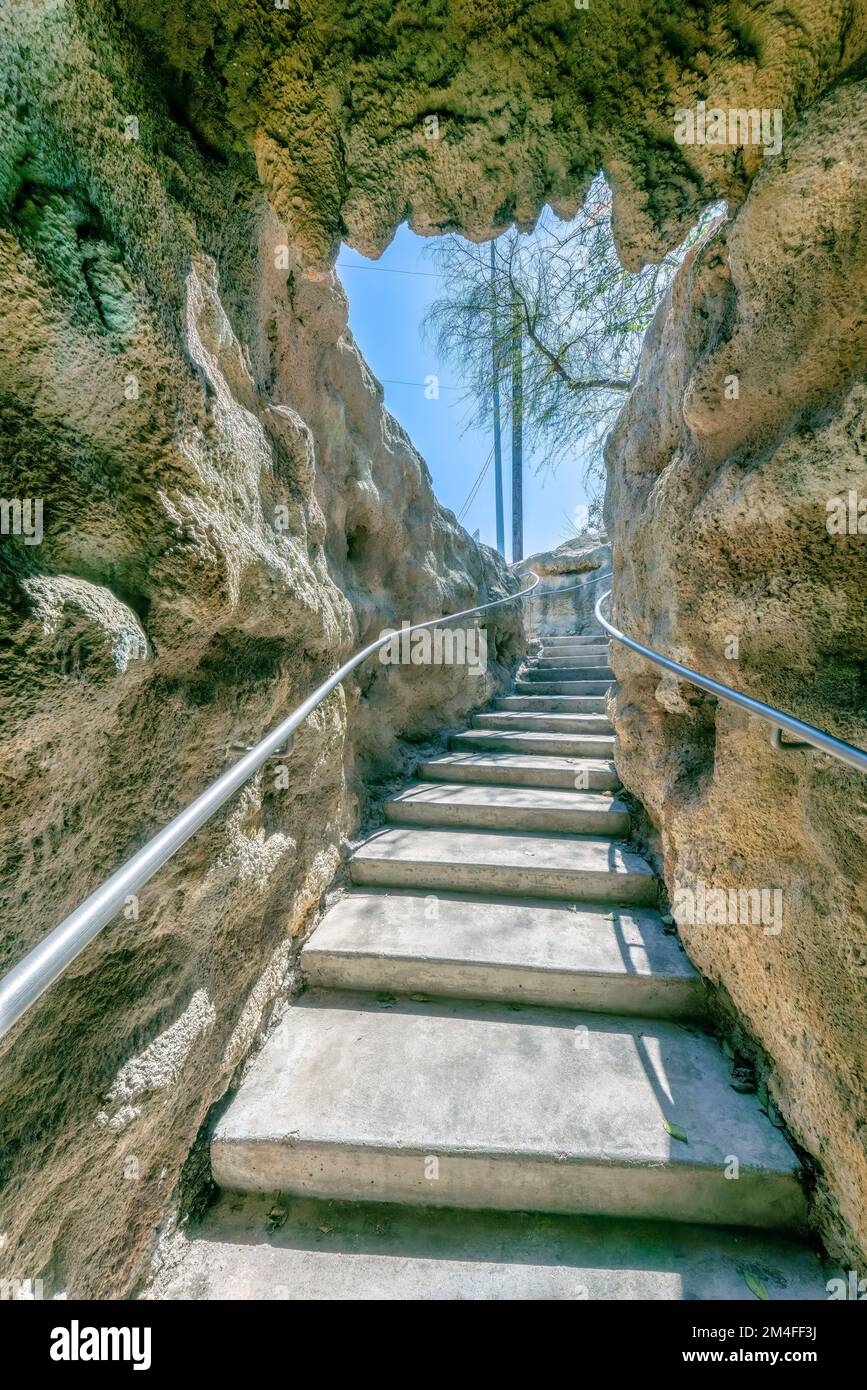 San Antonio, Texas – schmale Treppe in einer künstlichen Höhle mit an der Wand befestigten Handläufen. Weg nach draußen mit blattlosen Bäumen und Pfosten gegen die Stockfoto