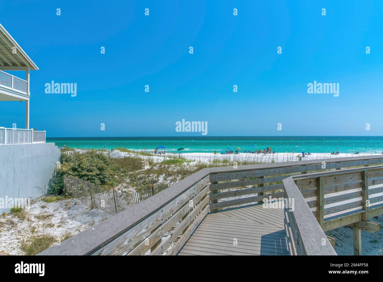 Blick auf den Strand mit Touristen am Ufer von einer Promenade in Destin, Florida. Es gibt einen Blick auf ein Strandhaus auf der linken Seite mit Balkonen in der Nähe des Stockfoto