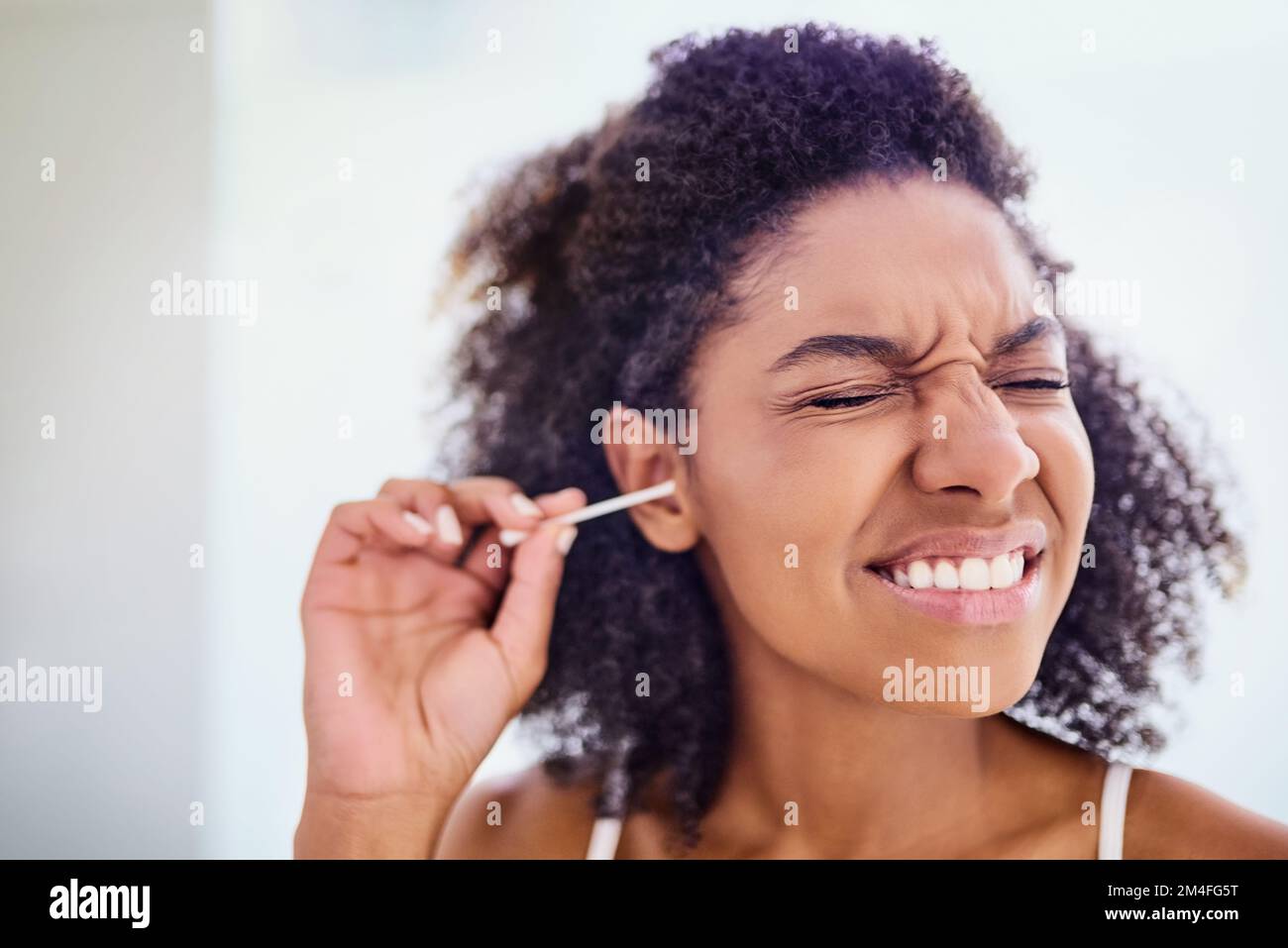 Ich komme gleich rein. Eine attraktive junge Frau, die sich während ihrer Morgenroutine zu Hause mit einem Wattestäbchen die Ohren putzt. Stockfoto