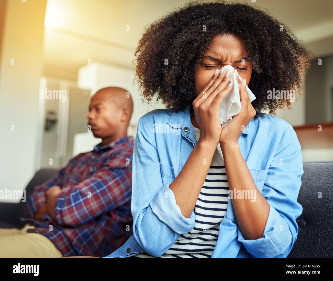 Ich hasse es, an solchen Tagen krank zu sein. Eine unbehagliche junge Frau, die in ein Taschentuch niest, während sie zu Hause auf einer Couch sitzt. Stockfoto