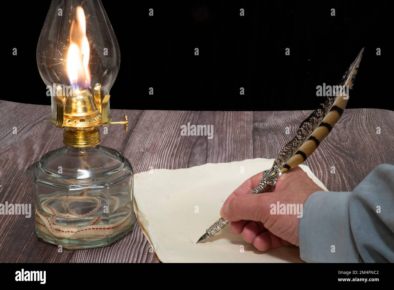 Nahaufnahme einer Öllampe und einer Person, die mit einem Kugelschreiber auf dem Papier schreibt Stockfoto