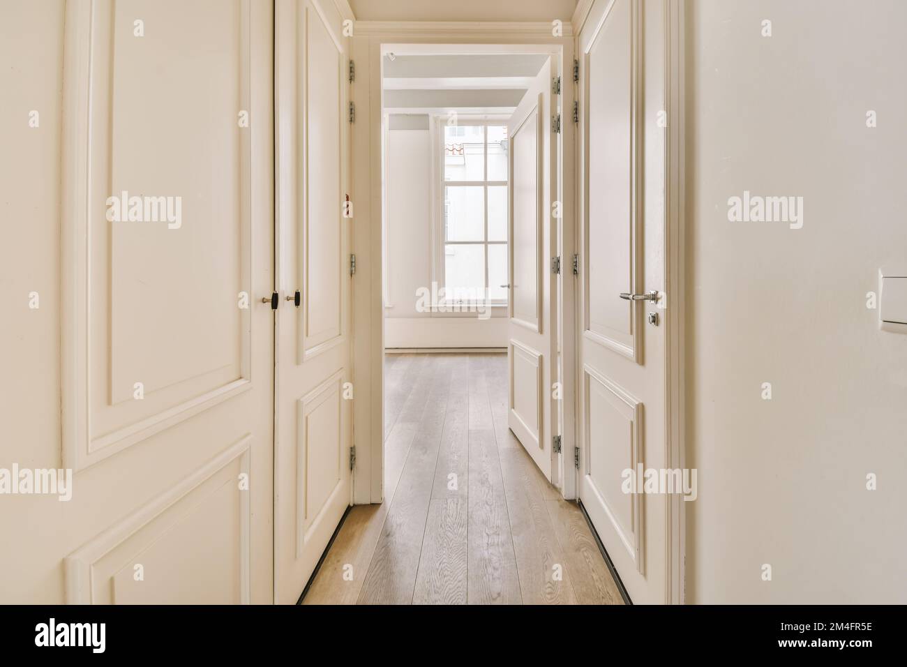 Ein langer Flur mit weißen Wänden und Holzfußboden auf jeder Seite, der zu den anderen Zimmern führt Stockfoto