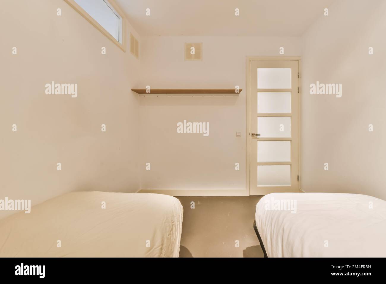 Zwei Betten in einem Zimmer mit weißen Wänden und Holzregalen an der Wand auf der rechten Seite sind eine offene Tür Stockfoto