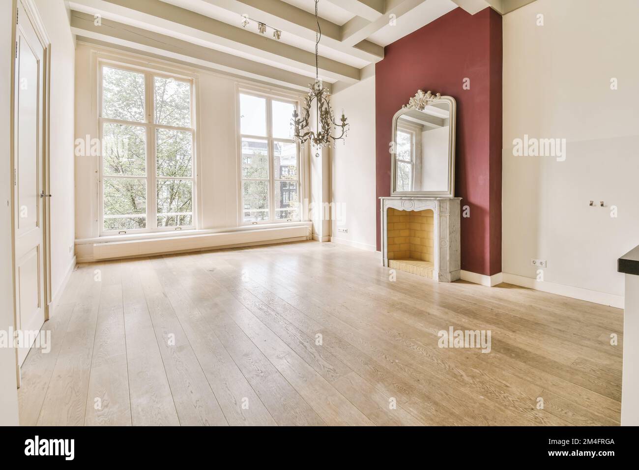 Ein leeres Wohnzimmer mit Holzfußboden und rot bemalten Wänden, weiße Verzierungen um das Fenster herum Stockfoto