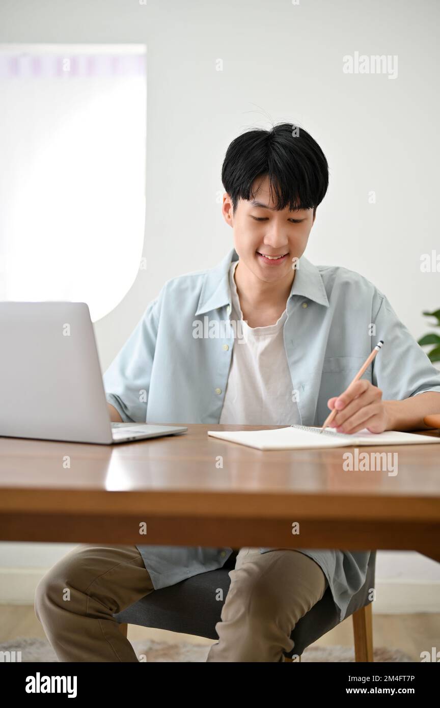 Porträt, gutaussehender junger, männlicher asiatischer Student, der Hausaufgaben macht, Notizen macht oder Listen auf einer Zeitung macht. Stockfoto