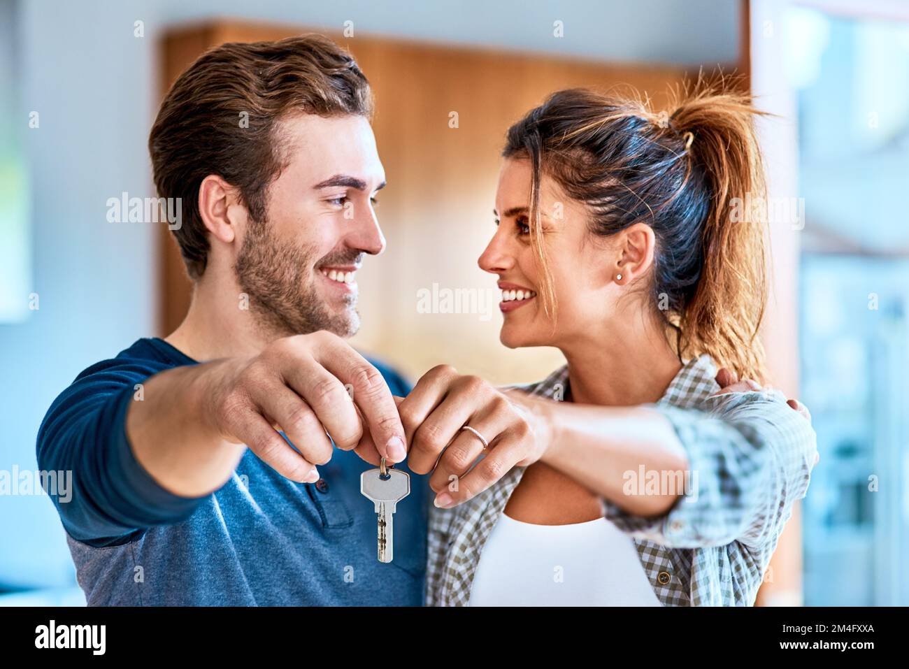 Unser neues Leben beginnt jetzt. Ein fröhliches junges Paar, das tagsüber im Haus steht und einen Schlüssel zu seinem neuen Zuhause hält. Stockfoto