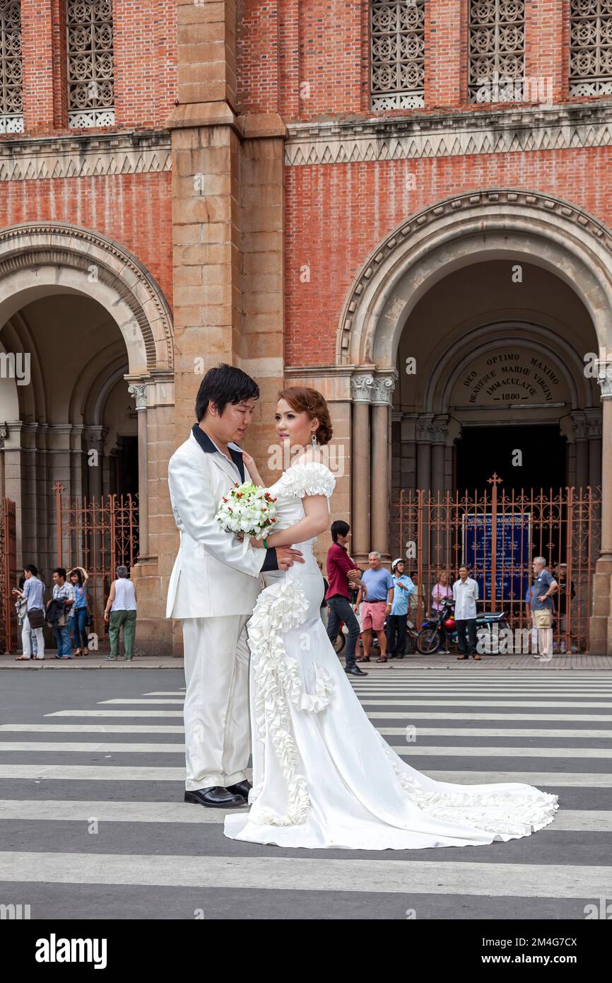 Vietnamesisches Paar, das sich für ein Hochzeitsfoto in weißer Kleidung posiert, vor der Kathedrale Notre Dame, Saigon, Vietnamp Stockfoto