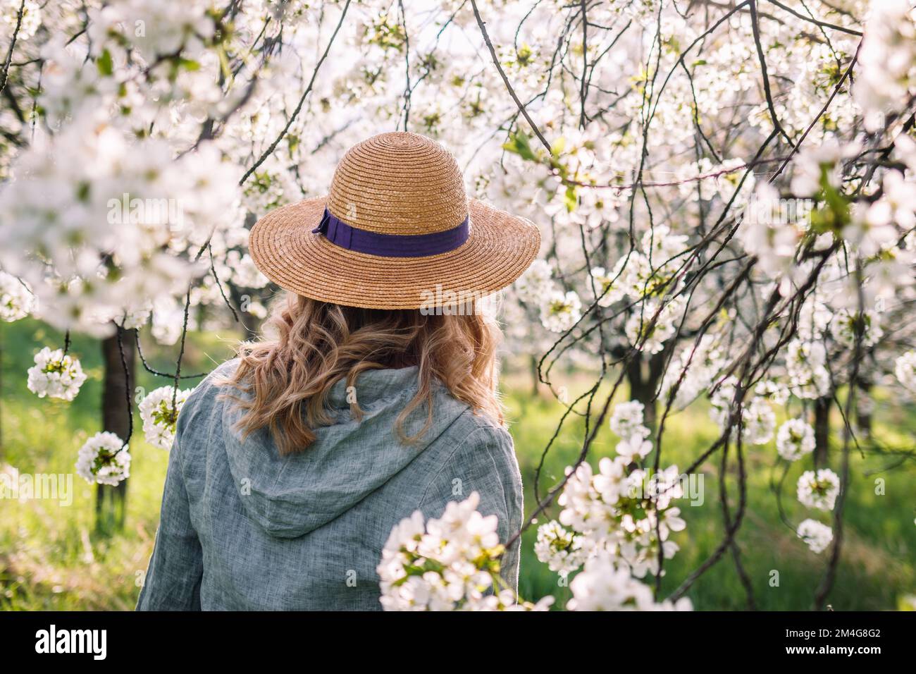 Frau mit Leinenhemd und Strohhut in blühendem Obstgarten. Genießen Sie den Frühling im Freien. Boho-Mode-Style Stockfoto