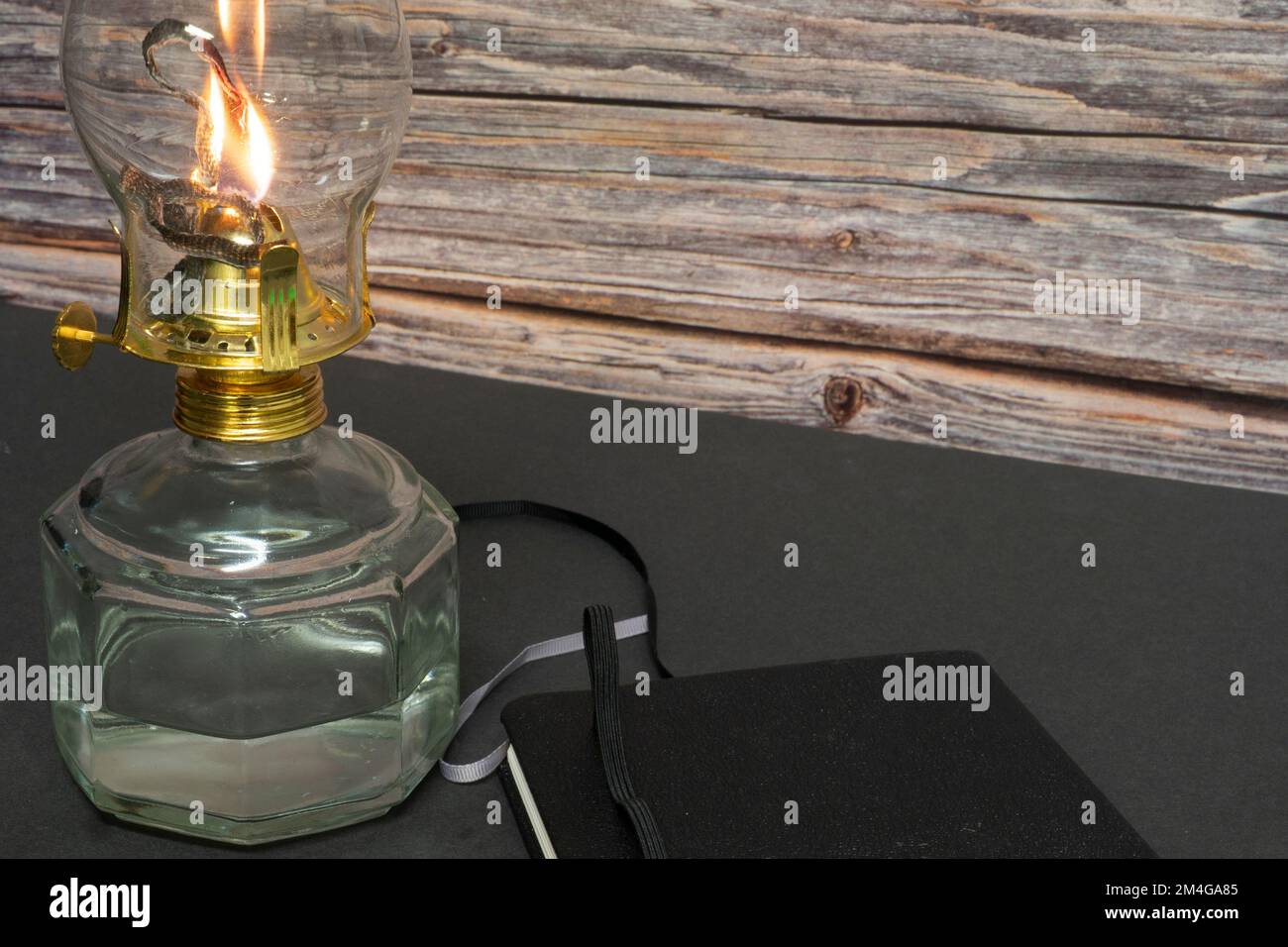 Eine Nahaufnahme einer brennenden alten Hurrikan-Öllampe mit geschlossenem Buch auf einem Holztisch Stockfoto