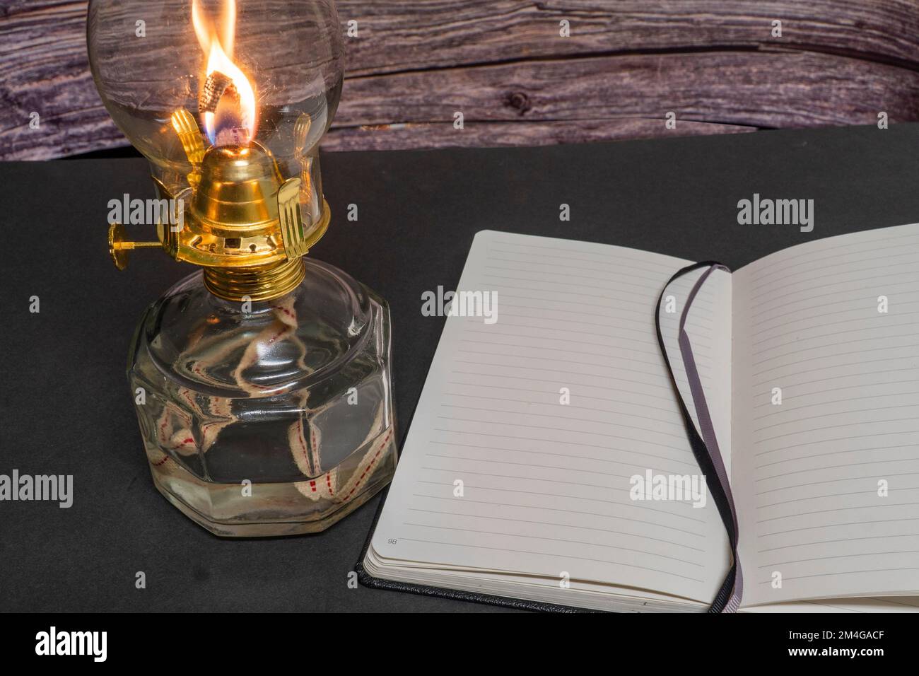 Eine Nahaufnahme einer brennenden alten Hurrikan-Öllampe mit offenem Buch auf einem Holztisch Stockfoto