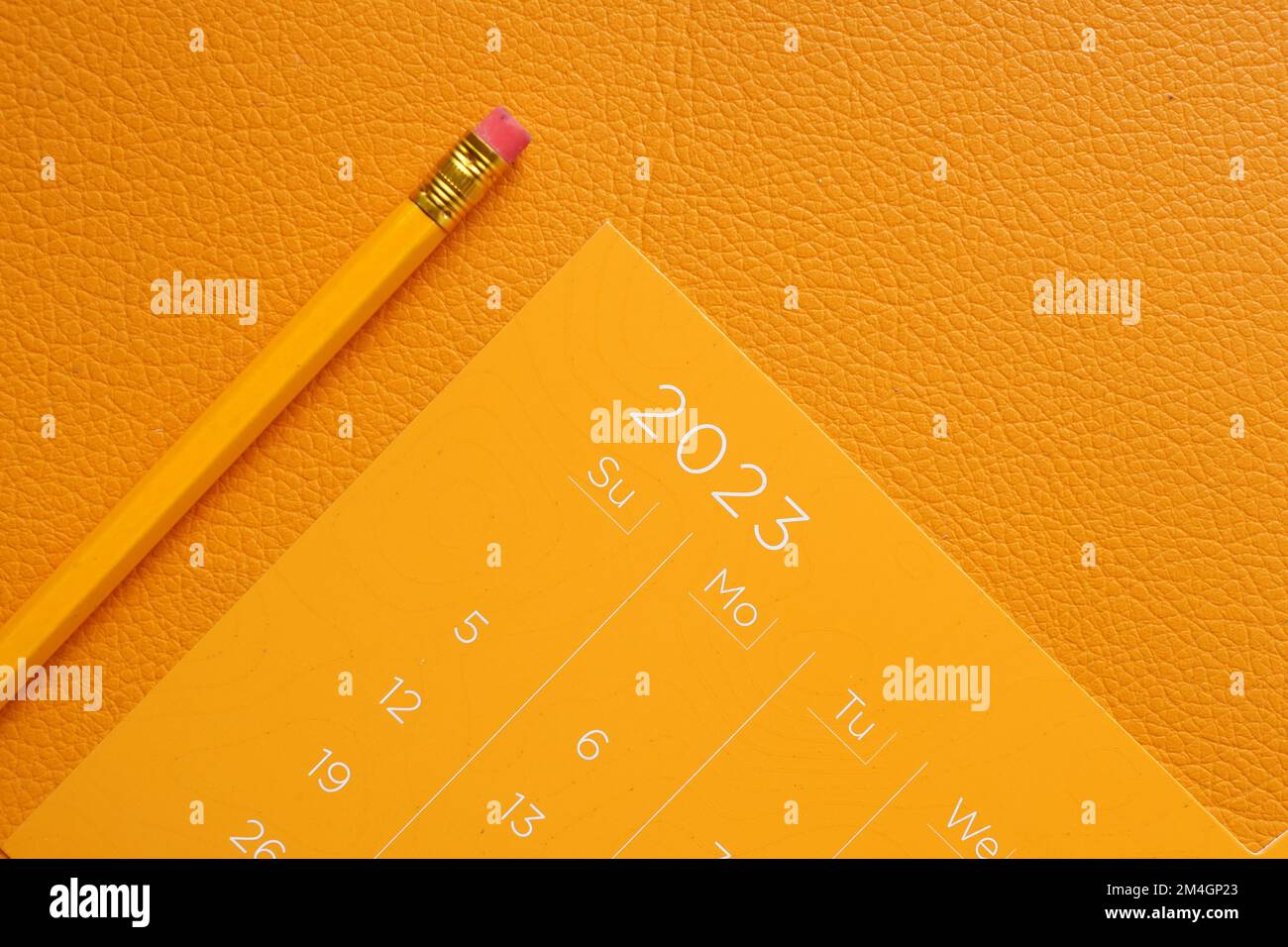 Orangefarbener 2023-Jahres-Kalender und Bleistift auf dem Tisch Stockfoto