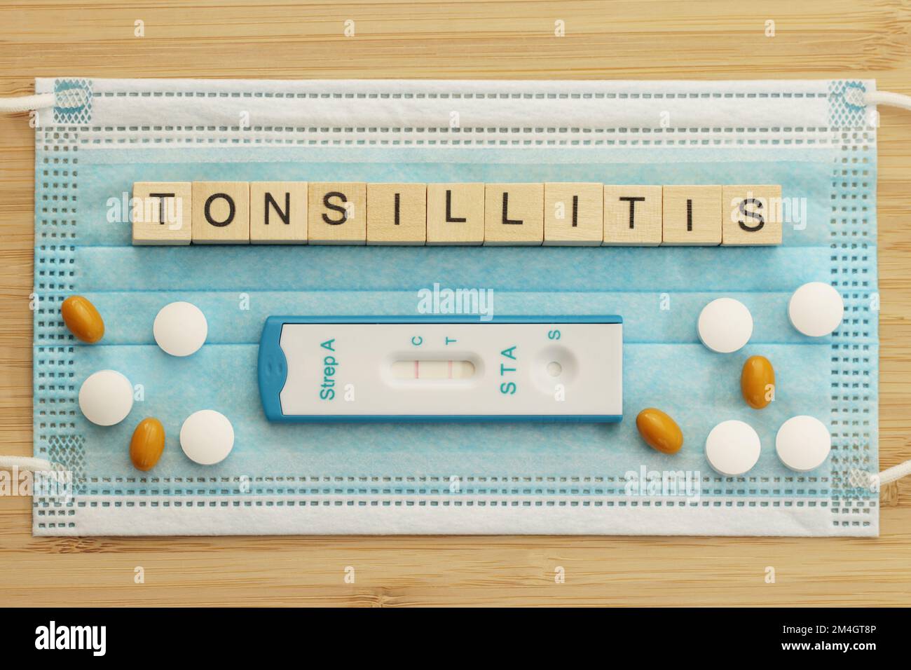 Das Wort Tolsillitis ist mit Holzwürfeln auf einer chirurgischen Gesichtsmaske gefüttert. Diese bakterielle Erkrankung wird durch Streptokokken verursacht. Ein Schnelltest für Gruppe A st Stockfoto