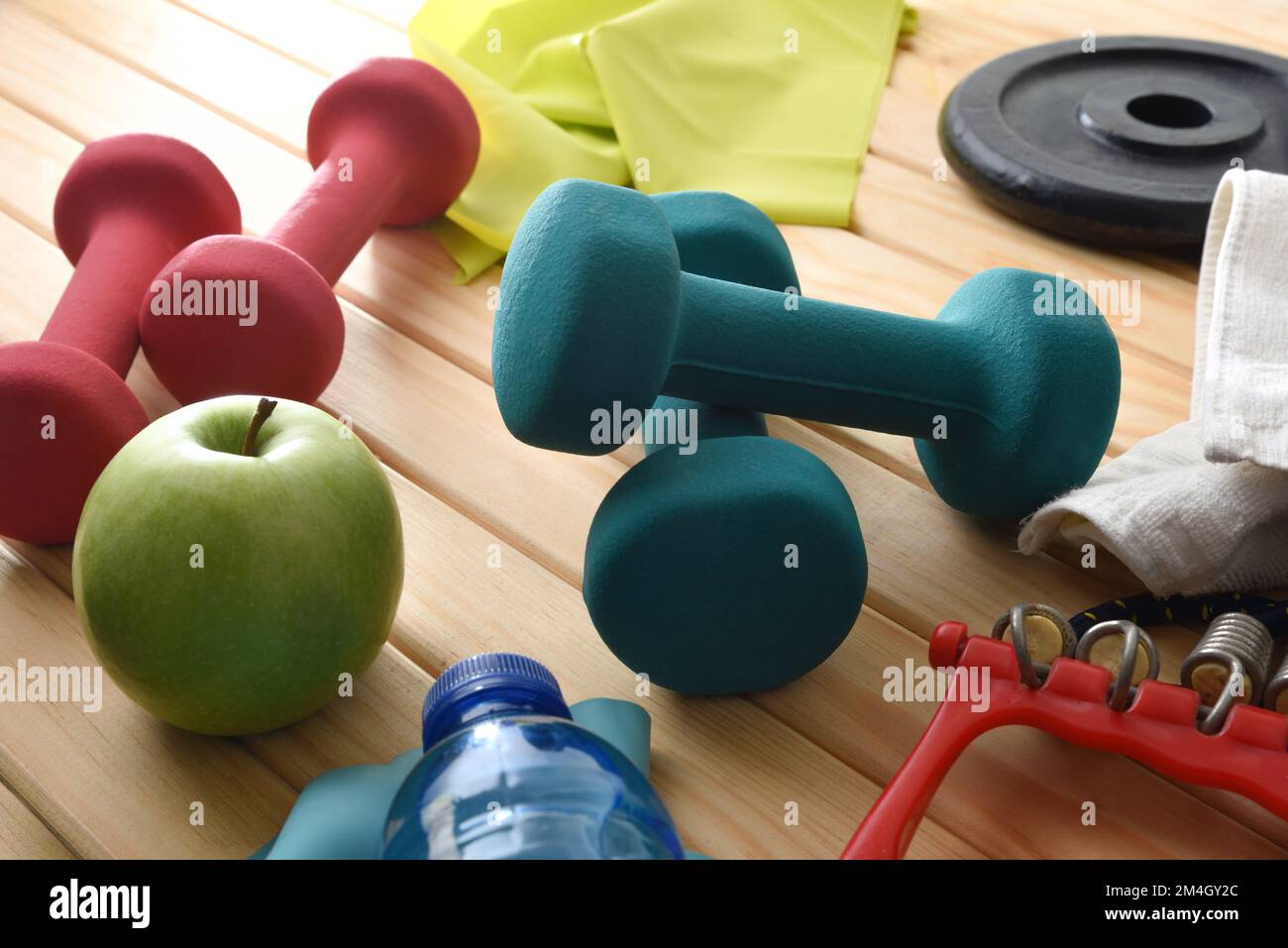 Hintergrund der Sportausrüstung und ein gesundes Wohnen auf einem Holzboden mit Kurzhanteln, Gewichten, elastischen Bändern und gesunder Ernährung. Erhöhte Aussicht. Stockfoto