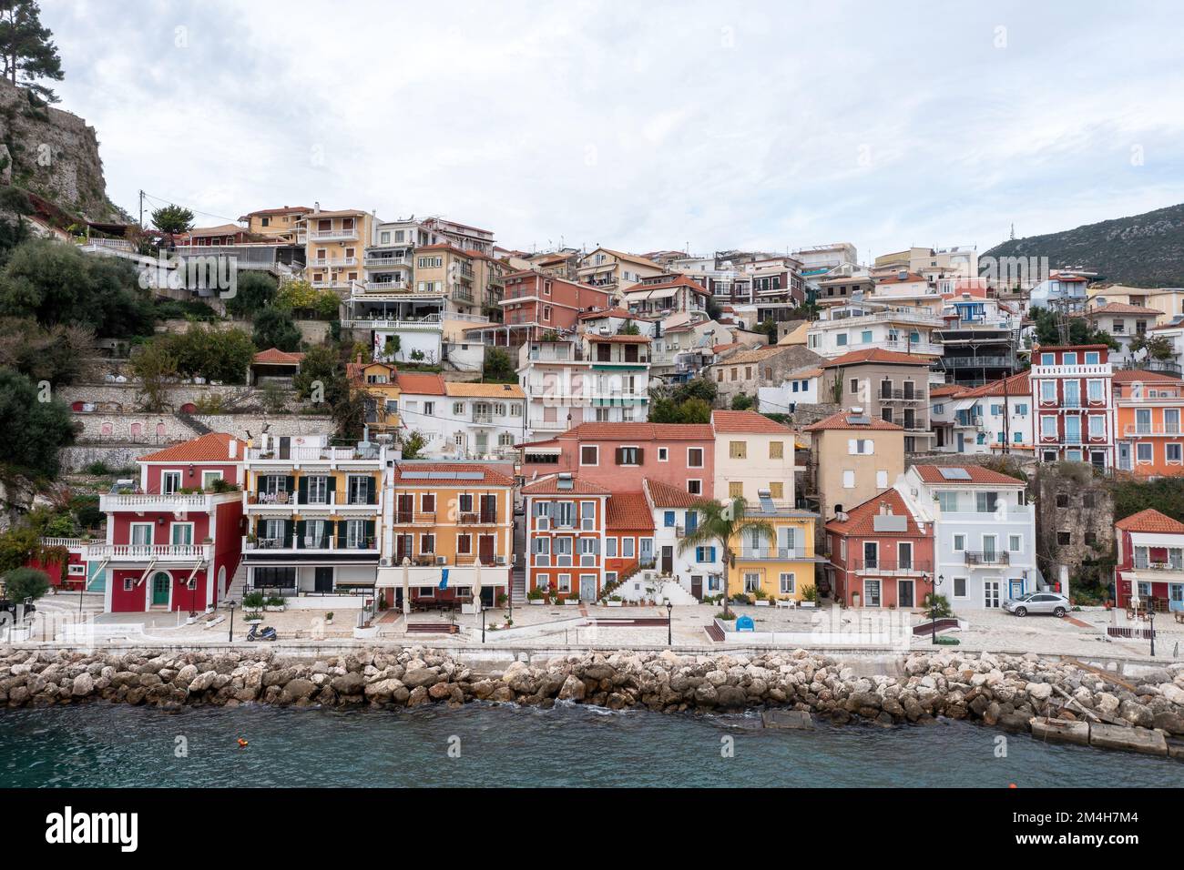 Parga, Griechenland. Traditionelle Stadt an der Ionischen Küste mit farbenfroher Fassade am Wasser gelegene Gebäude auf dem Hügel, wolkiger Himmel im Hintergrund. Stockfoto