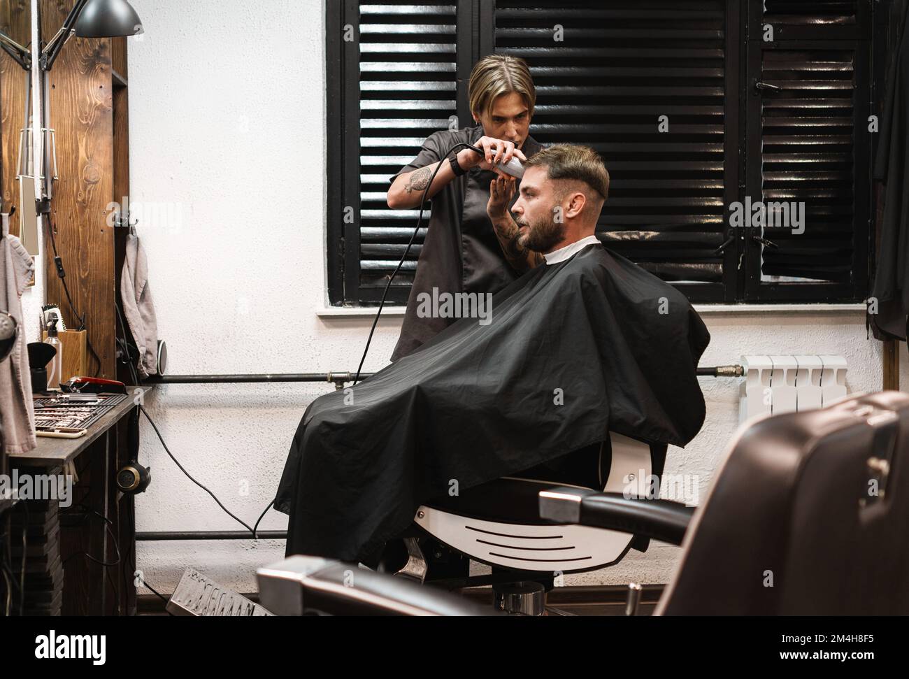 Friseurin schneidet Haare an Mann mit Trimmer im Friseursalon, echte Kunden und Friseur. Stockfoto