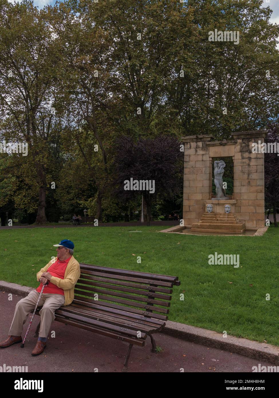 Man sentado en un banco del parque Fuente con rostros y escultura en el Jardín del Museo de Bellas Artes de Bilbao España, Europa. Stockfoto