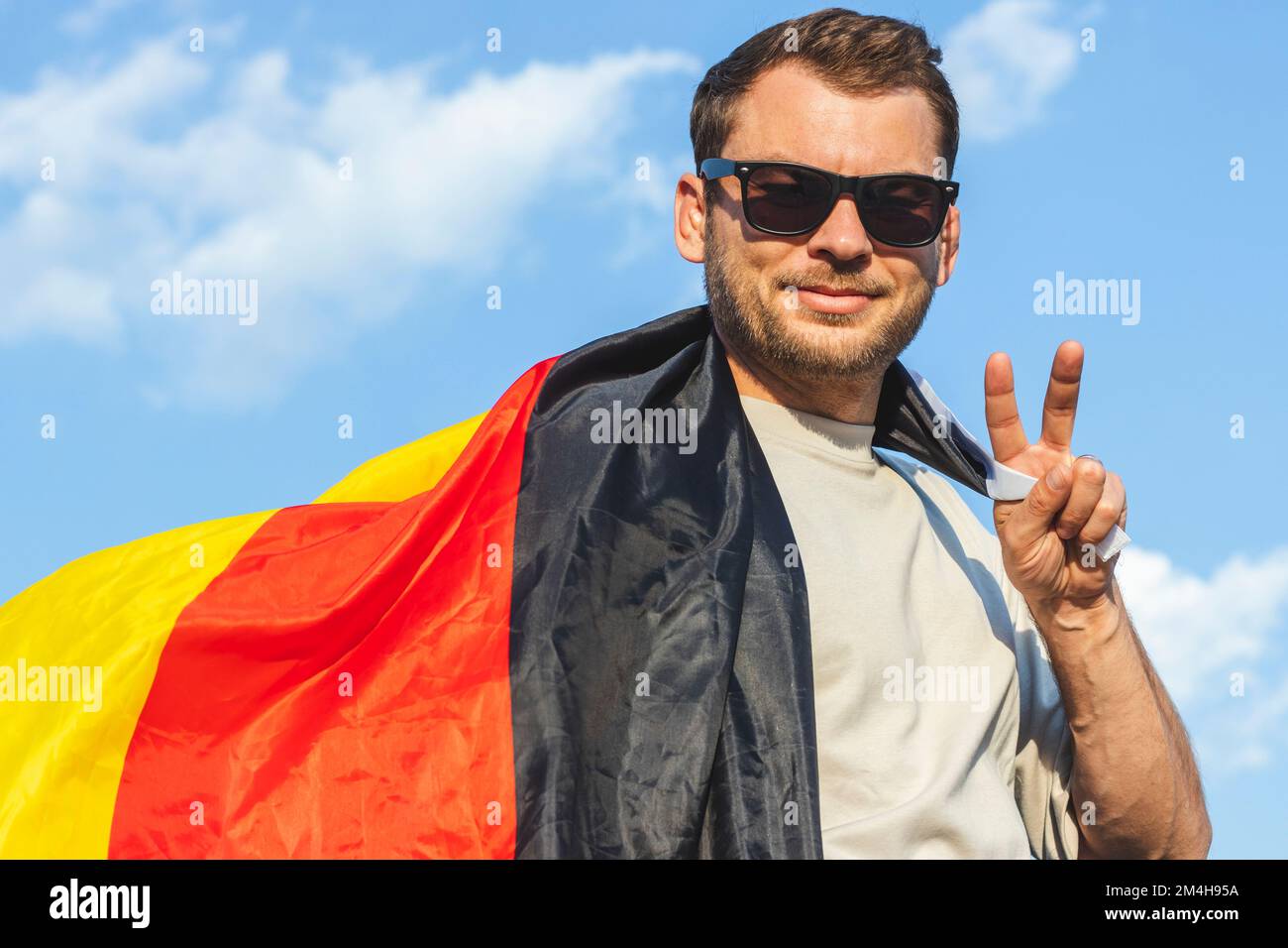Ein Mann mit deutscher Flagge, der mit den Fingern ein Siegeszeichen zeigt. Stockfoto