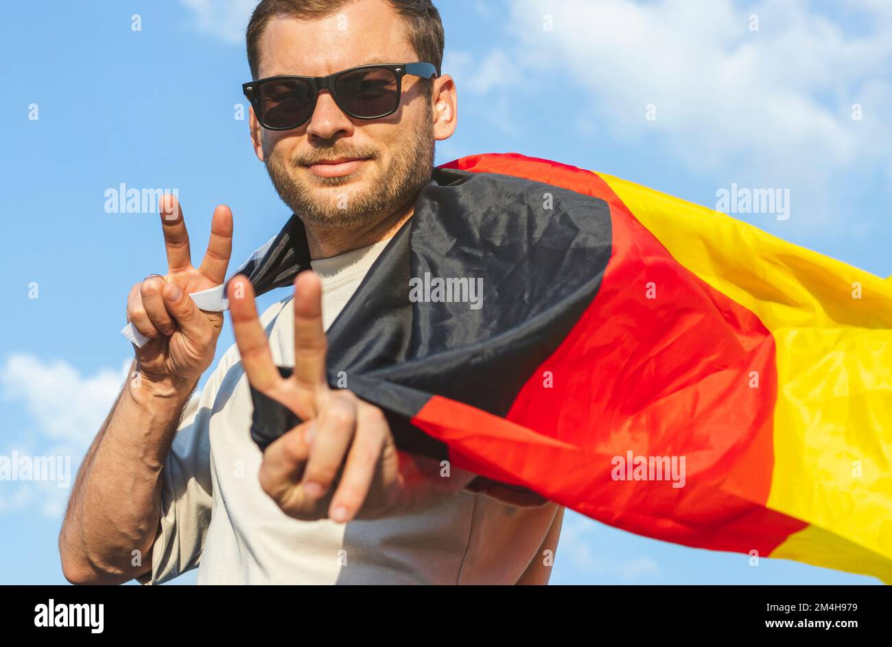 Ein Mann mit deutscher Flagge, der mit den Fingern ein Siegeszeichen zeigt. Stockfoto