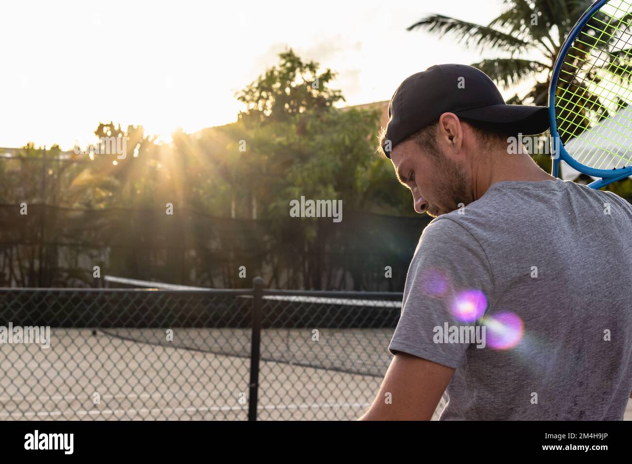 Männlicher Tennisspieler steht auf dem Tennisplatz im Freien mit einem Schläger auf der Schulter und schaut nach unten. Stockfoto