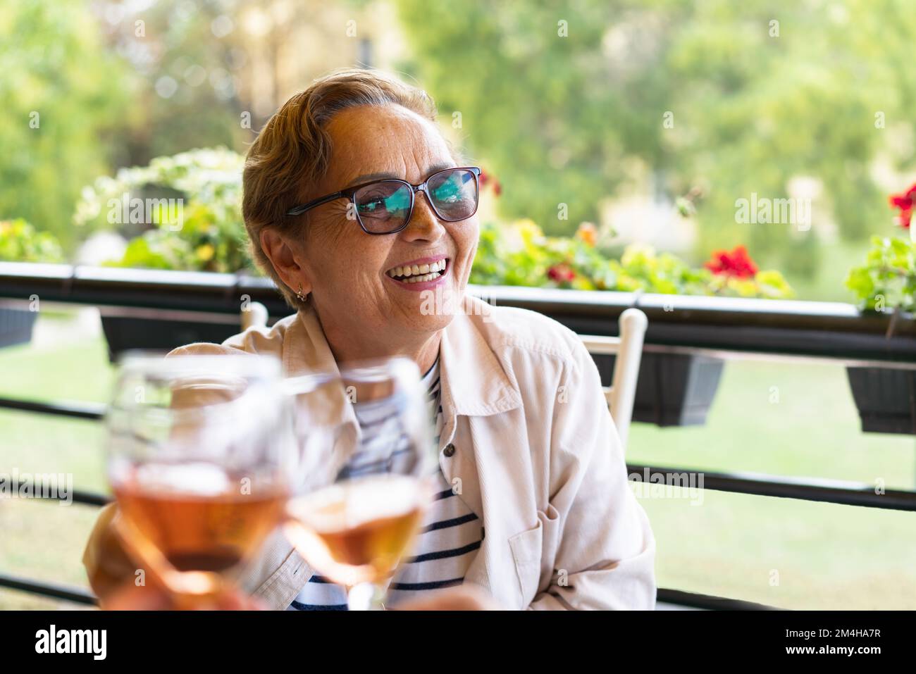 Fröhliche ältere Frau, die auf der Terrasse des Cafés mit einer Weingläserin klimpert. Muttertag-Feier. Stockfoto