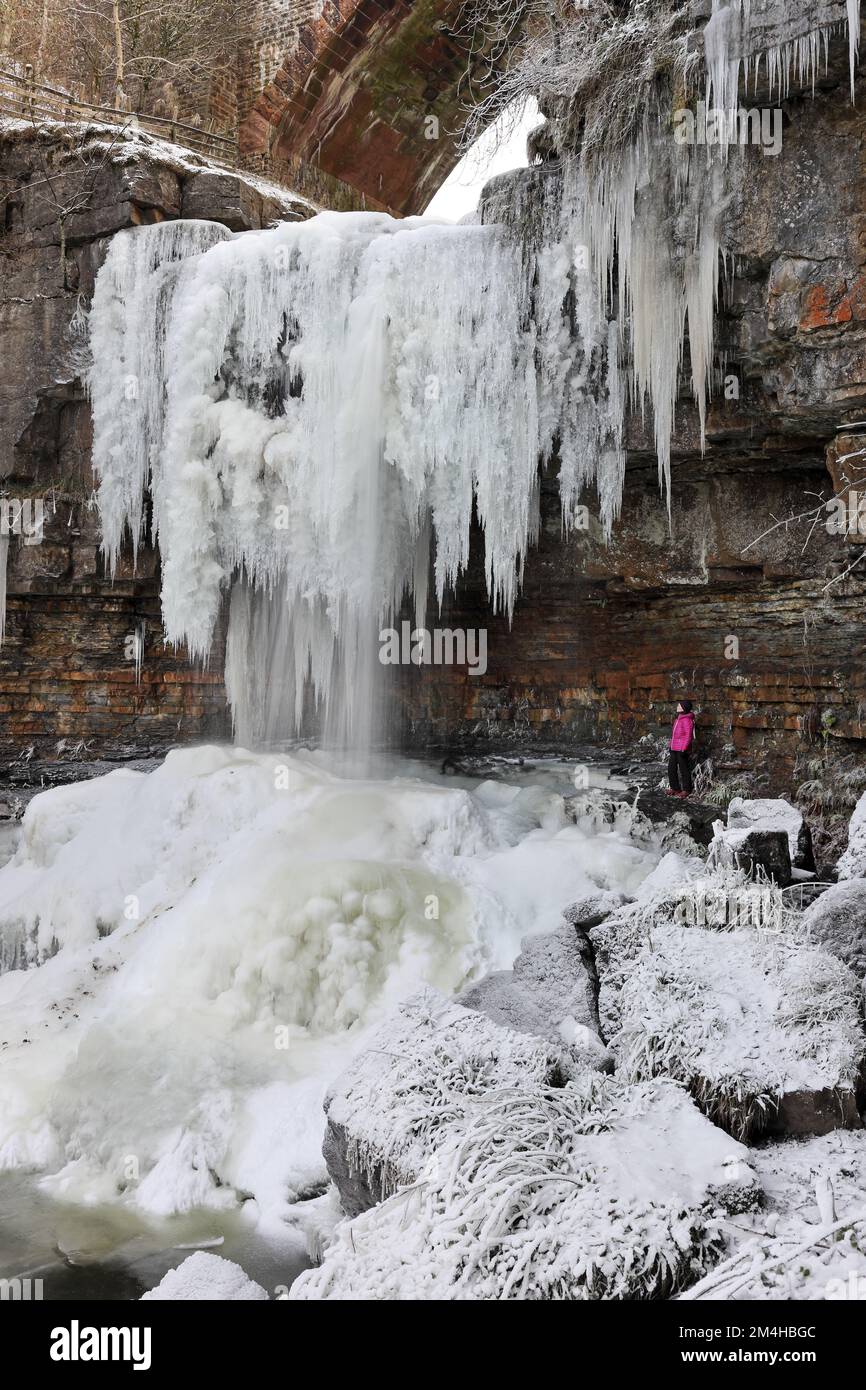 Ein Wanderer, der das Spektakel der riesigen Eiszapfen am gefrorenen Wasserfall der Ashgill Force in der Nähe von Garrigill, Cumbria, Großbritannien, genießt Stockfoto