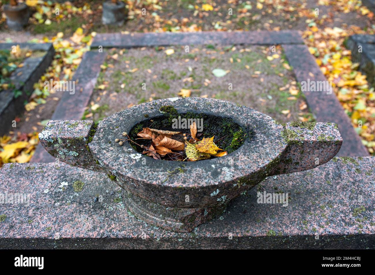 Grabstein oder Grabstein oder Grabstein mit herabfallenden Blättern im Herbst. Hietaniemi Friedhof, Helsinki, Finnland. Stockfoto